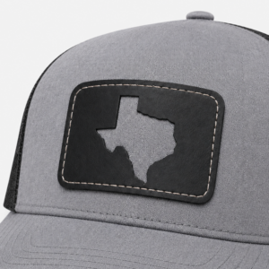 Close-up of the Texas Cutout Patch Trucker Hat featuring a black leather patch with a Texas-shaped cutout on gray fabric