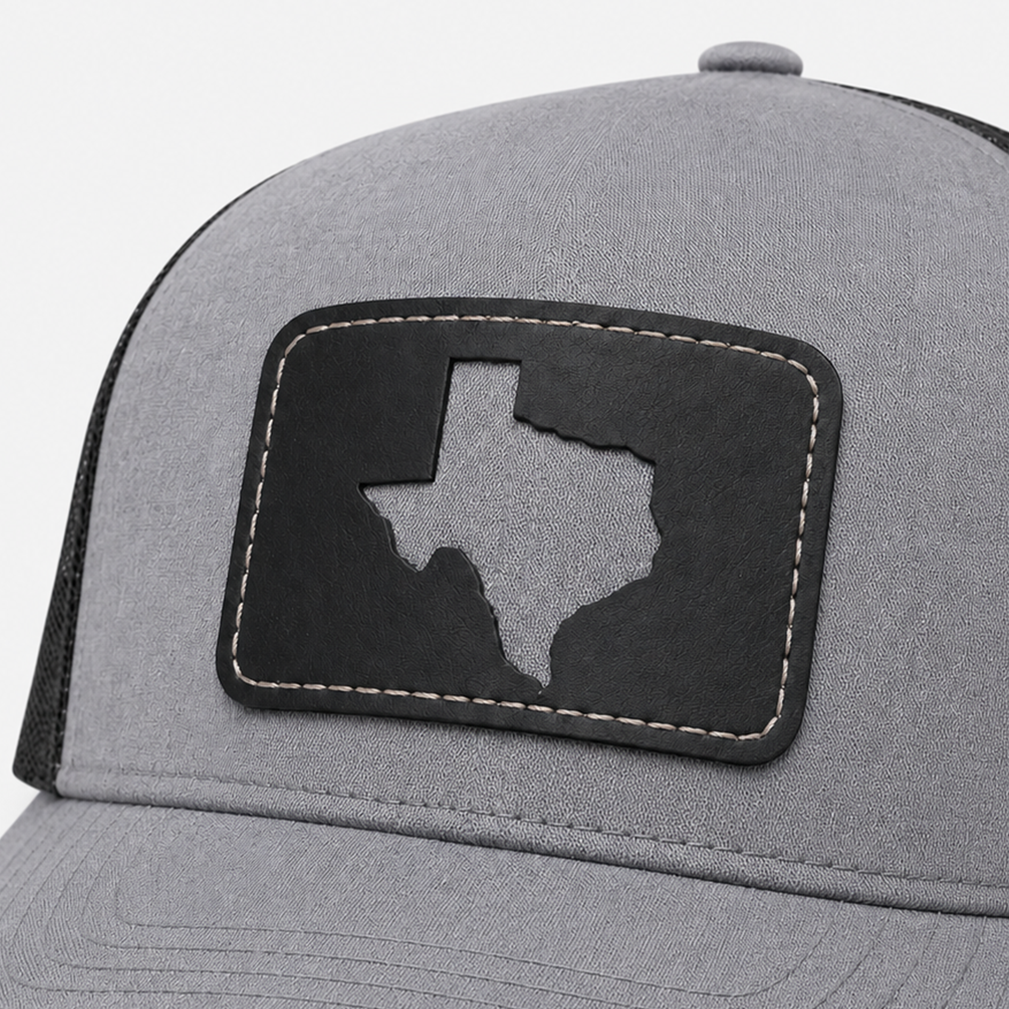 Close-up of the Texas Cutout Patch Trucker Hat featuring a black leather patch with a Texas-shaped cutout on gray fabric