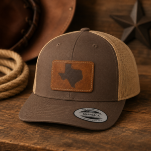 Texas Engraved Patch Trucker Hat displayed on a rustic wood background with western-style props.